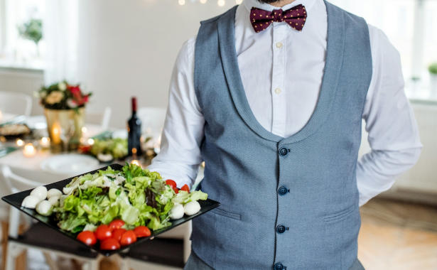 Servant with blue waistcoat serving a plate of nutritious vegetable salad